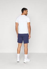 Camiseta blanca de manga corta combinada con pantalones cortos azul marino, zapatillas deportivas blancas y calcetines blancos. Diseño simple y ajustado sin patrones notables.