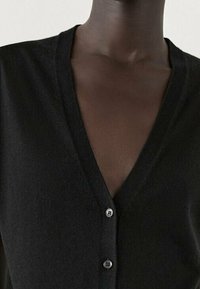 Schwarze V-Ausschnitt-Cardigan aus weichem Strickmaterial, mit einer Knopf-Front und zwei hellen Knöpfen sowie einer glatten Textur.