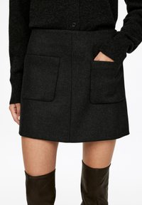 Grauer Woll-Minirock mit zwei vorderen Taschen, geradem Schnitt und sauberen Kanten, kombiniert mit knielangen braunen Lederstiefeln.