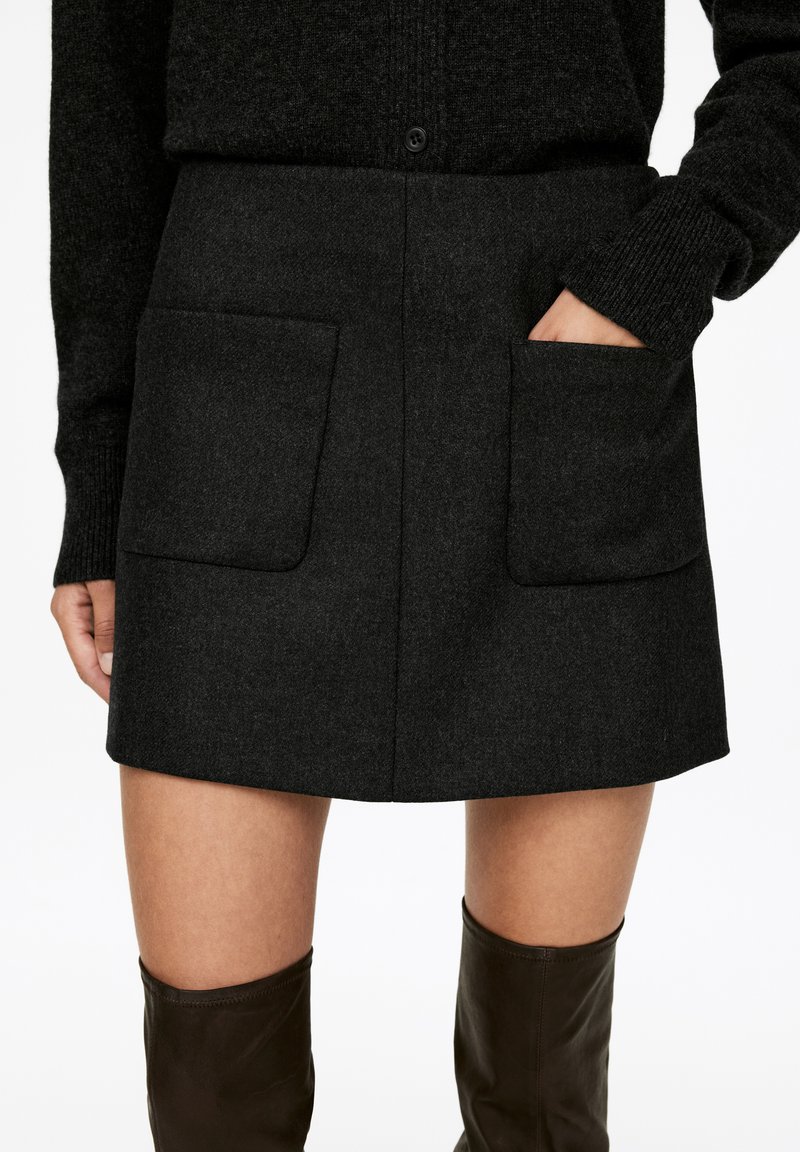 Grauer Woll-Minirock mit zwei vorderen Taschen, geradem Schnitt und sauberen Kanten, kombiniert mit knielangen braunen Lederstiefeln.