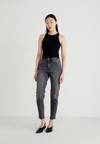 Melna bezmugura blouse, apvienota ar augsto vidukli, izbalējušām pelēkām džinsām. Šaura silueta un smalkas tekstūras detaļas. Melni, norādītas pirkstu kurpes pabeidz izskatu.