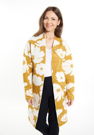 Sweter z otwartym przodem w kwiatowy wzór w musztardowym żółtym i białym kolorze, wykonany z miękkiego materiału. Posiada długie rękawy i luźny krój.