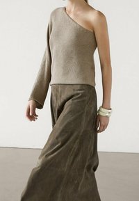 Haut beige en maille à une épaule associé à une longue jupe en cuir marron. La tenue présente une finition texturée et un style simple et moderne.