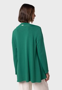 Grön långärmad topp med avslappnad passform, rund halsringning och subtila detaljer på baksidan. Slät textur, avslappnad design.