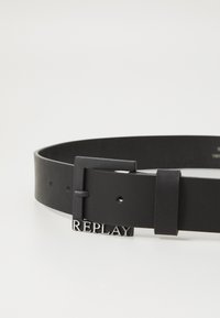Ceinture en cuir noir avec une finition mate, dotée d'une boucle rectangulaire et d'un logo "REPLAY" en relief. Réglable avec plusieurs trous.