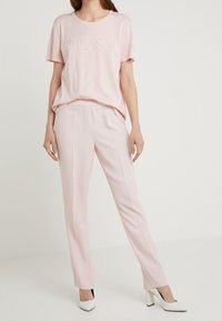 Light pink short-sleeve t-shirt with "DKNY" in studded detail, paired with light pink tailored pants and white high-heeled shoes.