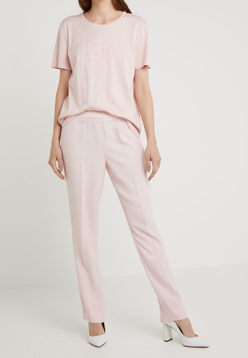 Light pink short-sleeve t-shirt with "DKNY" in studded detail, paired with light pink tailored pants and white high-heeled shoes.