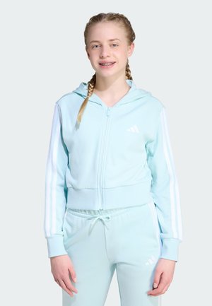 Felpa con zip atletica di colore azzurro chiaro con strisce bianche sulle maniche, abbinata a pantaloni jogger coordinati. Il tessuto sembra liscio ed elastico.