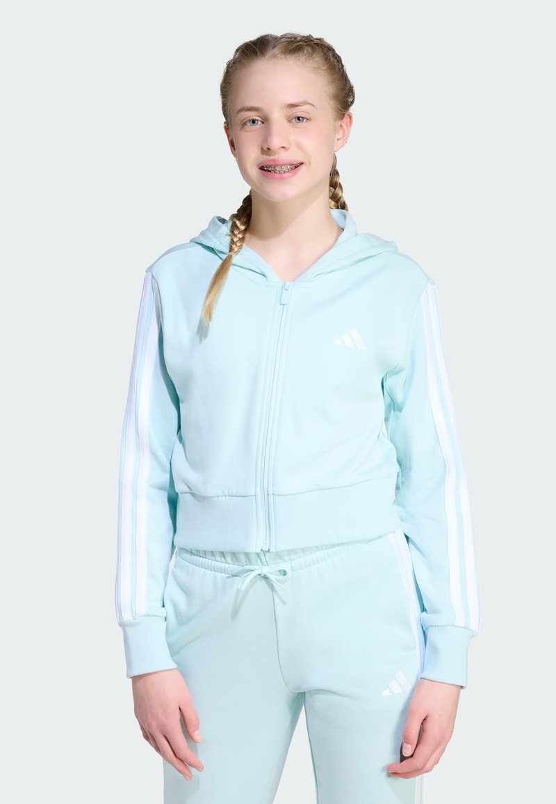 Sudadera deportiva azul claro con cremallera y rayas blancas en las mangas, combinada con joggers a juego. La tela parece suave y elástica.