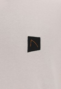 Suéter de punto color beige claro con un parche rectangular negro que presenta un diseño de líneas naranjas. Textura suave, diseño simple y minimalismo en los detalles.