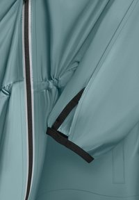 Veste bleu-vert claire avec une texture lisse, taille élastique et accents noirs ; dotée d'une fermeture zippée et d'un design de manches froncées.