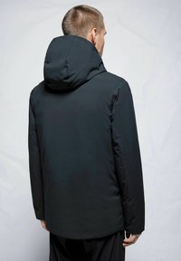 Chaqueta aislante negra con un cuello alto y capucha. Presenta un acabado suave y mate, así como una silueta simplificada.