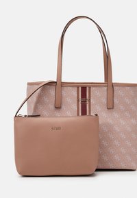 Vaaleanpunainen kantokassi, jossa on logokuvio ja punainen raita, yhdessä yhteensopivan vaaleanpunaisen vetoketjupussukan kanssa, molemmat varustettu kultaisilla yksityiskohdilla.