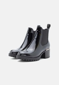 Černé lakované kotníkové boty na silném podpatku, s elastickými bočními panely a texturovanou gumovou podrážkou. Na oblasti podpatku se nachází zlatý akcent.