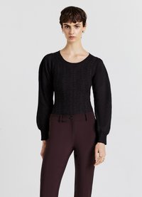 Maglione nero a maglia con motivo testurizzato, scollo rotondo e maniche lunghe a sbuffo. Abbinato a pantaloni attillati di un bordeaux scuro.