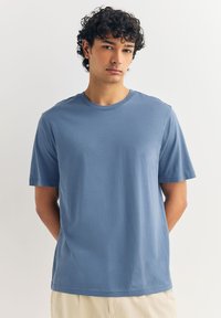 Plava majica kratkih rukava od mekog pamuka s okruglim izrezom, opuštenog kroja, glatke teksture, bez vidljivih uzoraka ili logotipa.