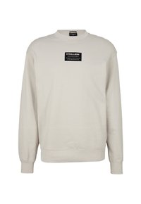 Sudadera beige clara de tejido suave con cuello redondo y mangas largas. Etiqueta rectangular negra en el frente.