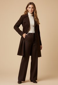 Brown corduroy trench coat with a tailored fit, buttoned front, and wide lapels, paired with cream turtleneck and brown wide-leg trousers.