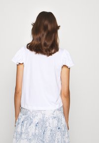 Vit bomull t-shirt med korta samlade ärmar, åtsittande design och rak fåll, i kombination med en svävande blåmönstrad kjol.