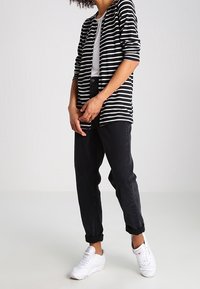Black and white striped cardigan over a white shirt, paired with dark rolled-up jeans and white sneakers. Smooth fabric texture, casual fit.