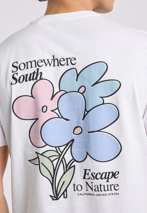 Witte T-shirt achterkant met grote pasteltinten bloemen en tekst met de woorden "Somewhere South Escape to Nature California United States."