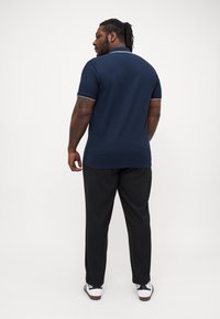 Cămașă polo navy cu dantele albe și mâneci scurte, asociată cu pantaloni negri și adidași albi. Material neted cu un design clasic.