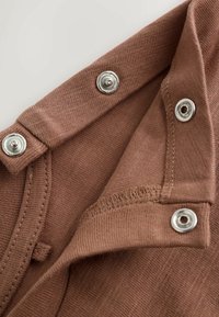 Close-up of brown fabric with silver snap button fasteners and visible stitching on a garment edge.