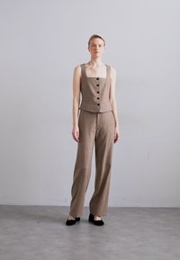 Top sin mangas marrón a medida con escote cuadrado y cinco botones frontales, combinado con pantalones anchos marrones. Tejido texturizado, diseño minimalista.