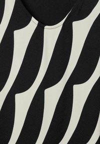 Tela negra y crema con patrones ondulados y en forma de ripples, textura suave y escote redondeado. Diseño ligero y fluido.