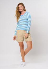 Blå og hvit stripete langermet topp paret med beige shorts, med en avslappet passform og elastisk midje, iført hvite joggesko.