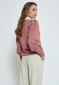 Pink knit sweater with puffed sleeves and ribbed cuffs, paired with beige tailored trousers, featuring side pockets.
