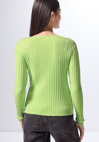 Maglione a maniche lunghe a coste di un vivace verde, con scollo ampio. Texture morbida e design aderente. Abbinato a jeans scuri.