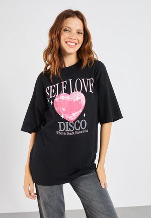 Črna oversized majica s kratkimi rokavi ima grafiko v obliki disko krogle v obliki rože in bele besede "SELF LOV DISCO" ter slogan.