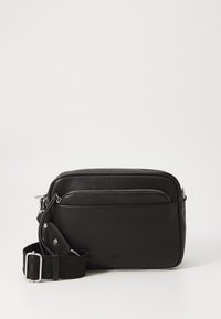 Sort læder crossover taske med tekstureret overflade, sølv lynlåse, justerbar stofrem og frontlomme med lynlås. Firkantet form.