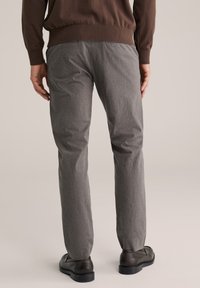 Szürke, texturált, egyenes szárú nadrág sötét cipővel és barna pulóverrel, hátulnézetben.