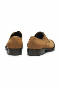 Paar braune Leder-Herrenschuhe mit schwarzen Sohlen, von hinten auf weißem Hintergrund dargestellt.