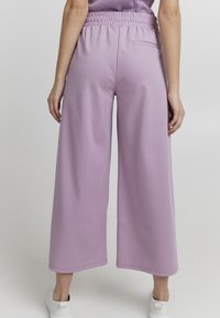 Fioletowe spodnie szerokie wykonane z miękkiego materiału, z elastycznym pasem i jedną tylną kieszenią, charakteryzujące się czystym dołem i luźnym krojem.