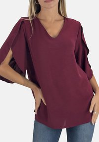 Top bordeaux con scollo a V e maniche corte a sbuffo. Realizzato in tessuto leggero, presenta dettagli di cuciture visibili e una vestibilità comoda.