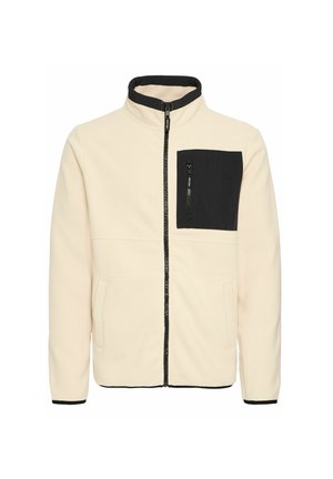 Veste en polaire crème avec une poche poitrine zippée noire, une fermeture éclair noire, un col montant et des poches latérales. Présente des finitions noires contrastantes.