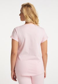 Rosa T-Shirt mit kurzen Ärmeln, rundem Halsausschnitt und hochgestellten Ärmeln. Weicher Stoff mit glatter Textur. Getragen mit passenden rosa Hosen.