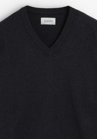 Pulover v-neck de culoare bleumarin închis, fabricat dintr-un material tricotat moale. Prezentă manșete și tiv cu striații. Eticheta spune "SCALPERS," mărimea L, cu un detaliu discret al logo-ului.