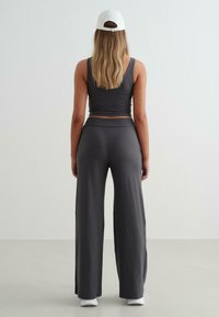 Szürke, rövidített tank top és puha anyagból készült, oldalán hasított széles szárú nadrág, fehér sportcipővel és fehér sapkával párosítva.