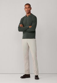 Tamnozeleni pleteni polo majica s ovratnikom i tri gumba, u kombinaciji s svijetlosmešavim hlačama i tamnosmešim cipelama.