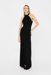 Zwarte halterjurk van zacht materiaal, met een gedrapeerd ontwerp, een getailleerde bustier en een hoge split tot aan de dij voor extra detail.