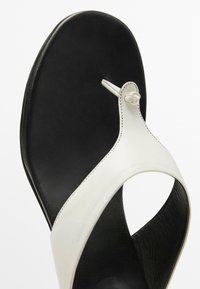 Schwarze und weiße Lederflip-Flops mit einer glatten schwarzen Sohle, einem weißen oberen Riemen mit Knoten-Detail und einer strukturierten schwarzen Innenseite.