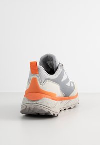 Szaro-biały but sportowy z pomarańczowym obcasem, teksturowaną podeszwą oraz wyściełanym kołnierzem. Posiada oddychającą siateczkową cholewkę oraz wzmocniony nosek.