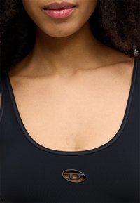 Čierne plavky s jemnou textúrou, širokým výstrihom a jemným leskom. Na strede sa nachádza malé čierne logo.