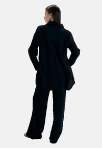 Camisa negra de manga larga texturizada con cuello, combinada con pantalones de pierna ancha. Ambos tienen un ajuste holgado y detalles sutiles.