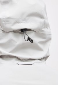 Οπίσθια όψη ενός ανοιχτό γκρι μπουφάν με κουκούλα, με ρυθμιζόμενο μαύρο κορδόνι και κούμπωμα στην κουκούλα.