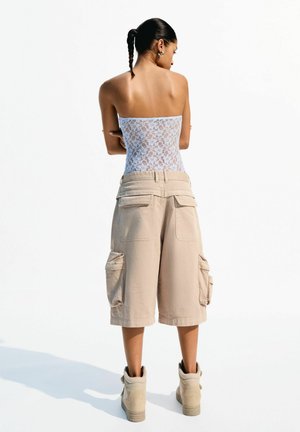 Strapless witte kanten top gecombineerd met beige cargoshorts met zijzakken, gedragen met beige hoge sneakers.